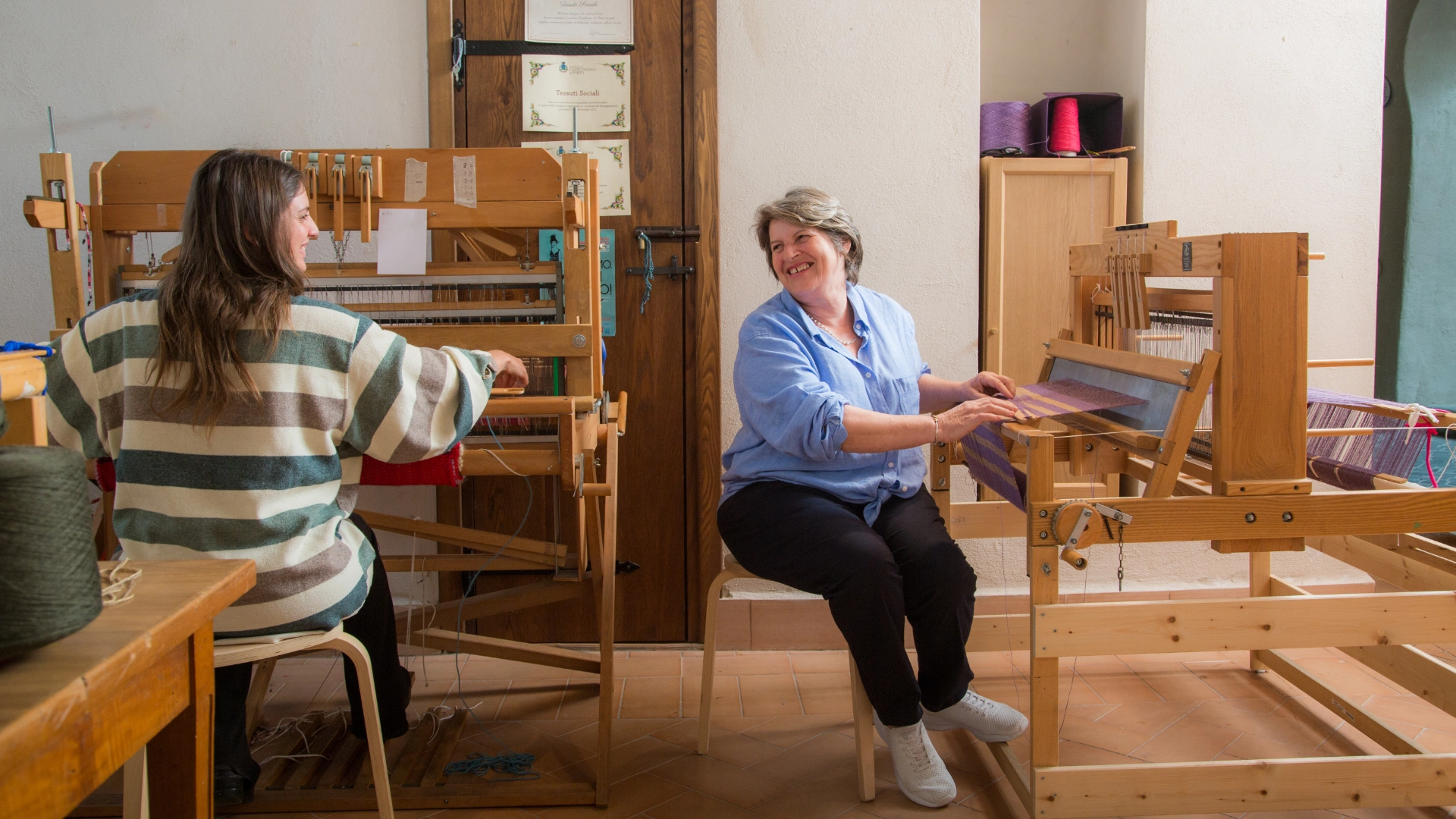 Foto di due donne che guardano sorridendo mentre lavorano al telaio