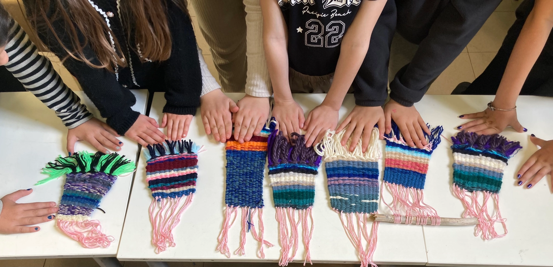 foto delle mani di tanti bambini poggiate a un banco con le loro realizzazioni in lana